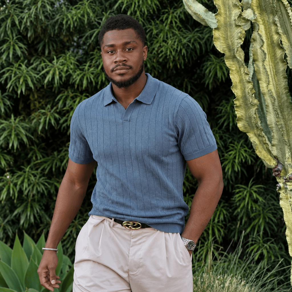 Man in a blue ribbed knit polo and cream trousers in a garden